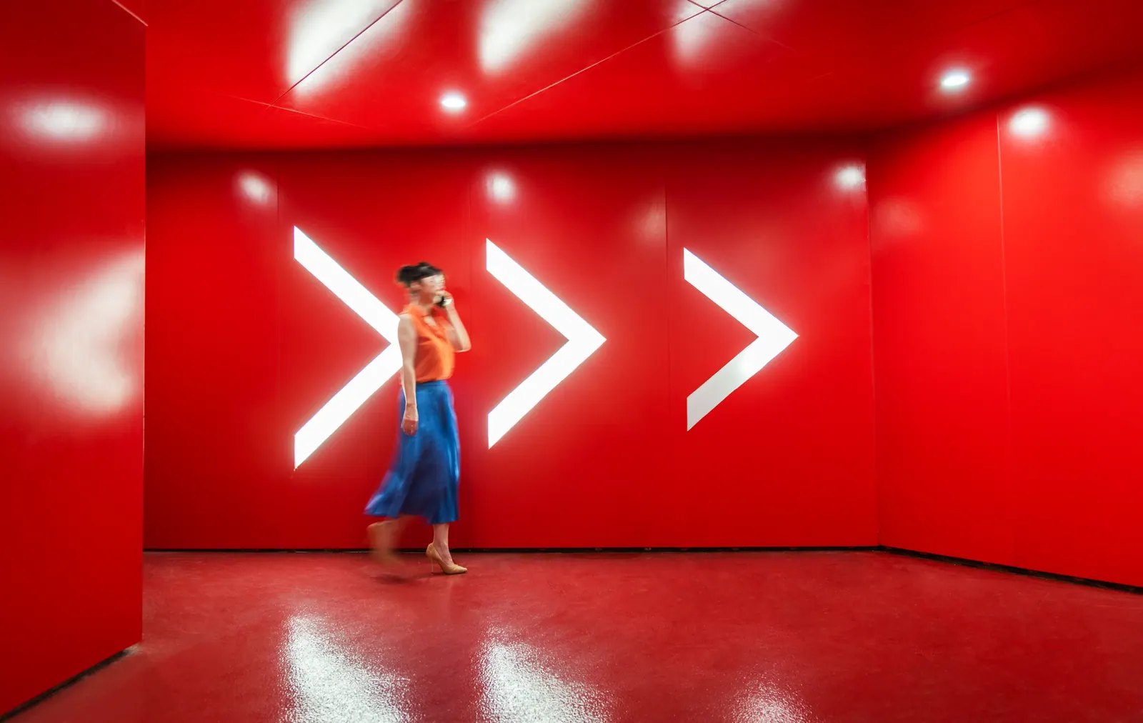 Woman walking past illuminated arrows in a red corridor