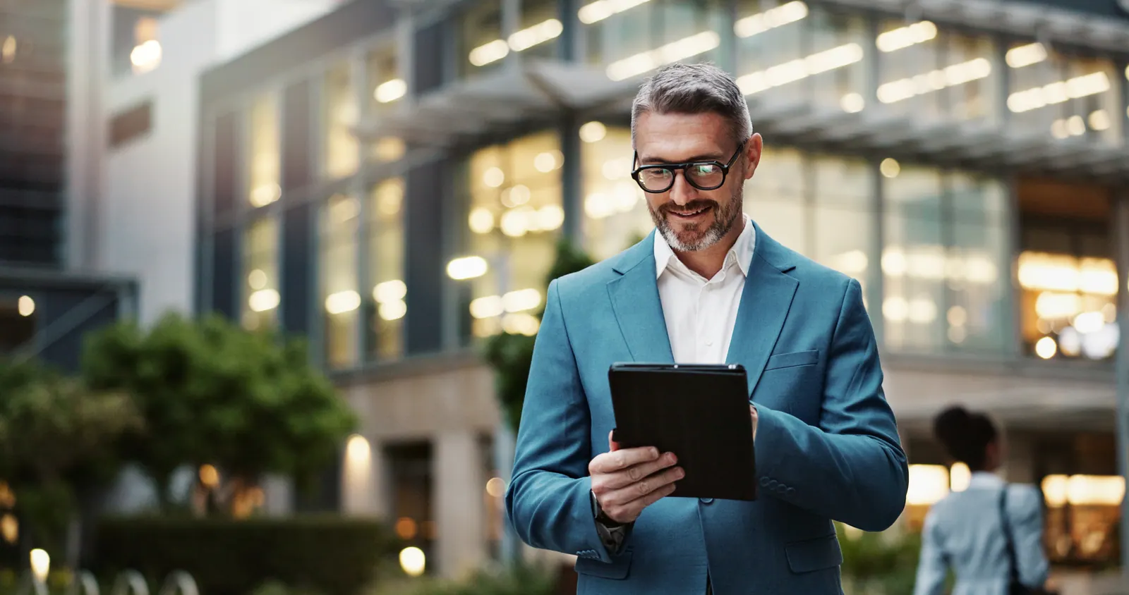 Man in a blue jacket using a tablet outside an office building